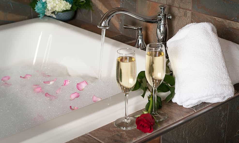 a bathtub with flowers floating on the water and two glasses of champagne enxt to it